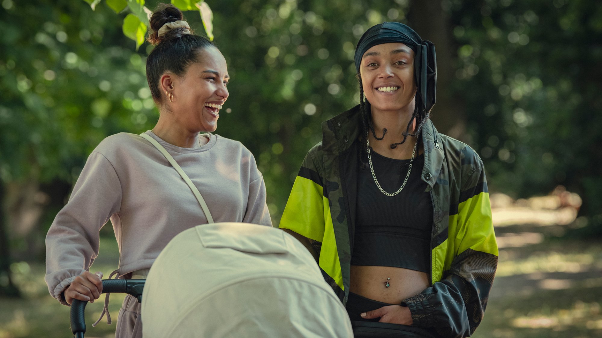Saffron Hocking and Jasmine Jobson walk through a park with a stroller, laughing, in the TV show "Top Boy"